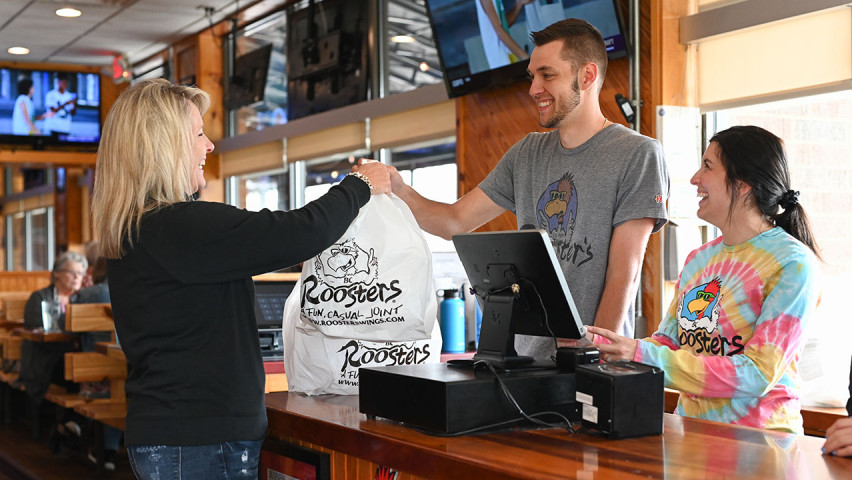 2 smiling Roosters employees handing off food to customer
